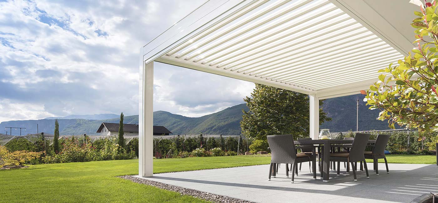 KE pergola covering a cement patio surrounded by green grass.